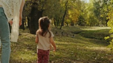 Genç bir anne ve küçük kızının yaz günü ördekleri besleme görüntüsü. Çocuk dışarıda kuşları besliyor. Küçük çocuklar için yaz etkinliği.