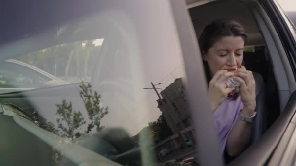 Молодая Голодная Женщина Ест Бургер Сидя Машине Путешествуя Перекусывая Дороге — стоковое видео