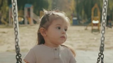 Küçük kız renkli bir salıncakta sallanıyor ve başka tarafa bakıyor. Mutluluk, özgürlük, keyif, sağlık. Parlak yaz günü.