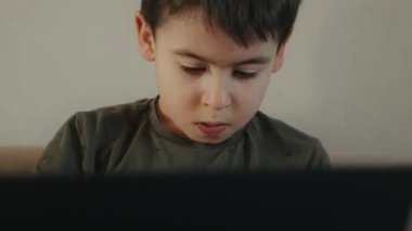 Kafkasyalı küçük çocuk evde tek başına oyun oynuyor. Kanepede oturuyor. Modern teknoloji ile kablosuz bilgisayar bağımlılığı kullanıyor. Eğitim, teknoloji ve insanlar