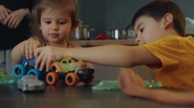 Bakıcısı evde, küçük kız kardeşiyle oturmuş araba oyuncakları oynayan küçük bir çocuk. Küçük çocuklar birlikte mutfak masasında oturarak eğleniyorlar.
