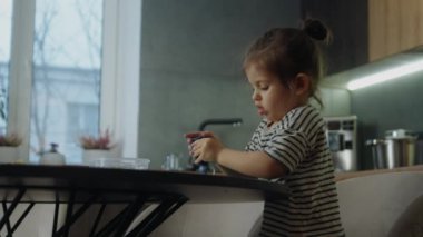Ev mutfağındaki masada çamurla oynayan küçük bir kız. Bebek için boş zaman aktivitesi, evlat. Duyusal ve yaratıcı becerilerin gelişimi.