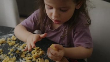 Küçük kız mutfak masasının üstünde hamur işleri pişirirken eğleniyor. Hafta sonu aile yemeği.