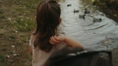 Yaz günü ördekleri besleyen küçük bir kızın arka görüntüsü. Çocuk dışarıda kuşları besliyor. Küçük çocuklar için yaz etkinliği.