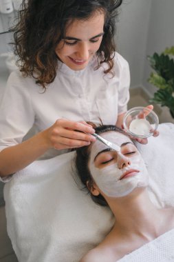 Güzellik uzmanının kilden maskesi olan güzel bir kadın. Rahatlatıcı tedavi ve ilaç konsepti