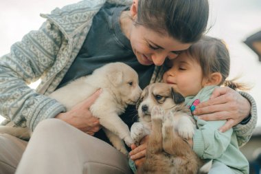 Yavru köpekleri okşayan küçük bir kız. Anne babasıyla evde eğleniyor. Çocuk için en iyi arkadaşlar. Hayvan konsepti olan aile.