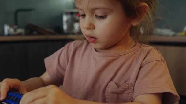 自宅でおもちゃの車で遊んでいる小さな女の子は 兄の近くのキッチンテーブルに座っていました 子供のための休日の活動 — ストック動画