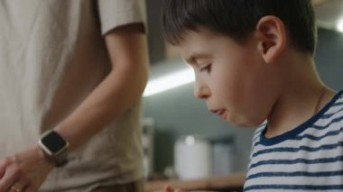 Komik küçük yardımcı çocuk mutfakta merdaneyle hamur yoğurmayı öğreniyor. Sevimli çocuk ve anne-baba kurabiye pişirirken eğleniyor. Aile, anne ve kız