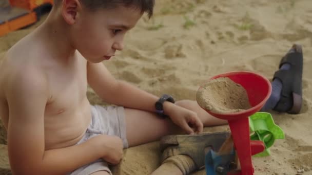 屋外の砂でコンストラクターのおもちゃで遊んでいるかわいい小さな慎重な少年 遊び場で楽しんでいる子供 — ストック動画