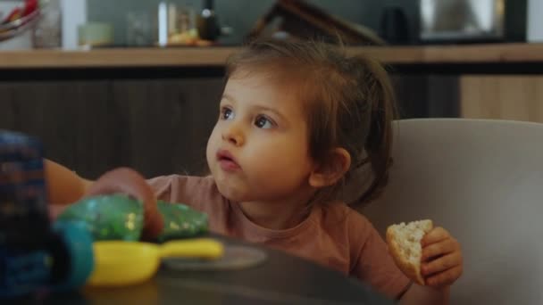 Porträtt Vacker Flicka Som Äter Bröd Medan Spelar Vid Köksbordet — Stockvideo