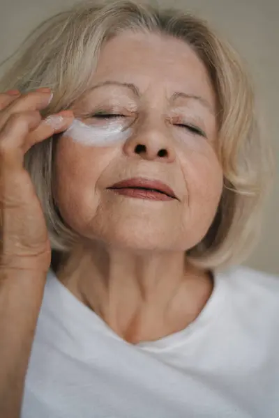Portrait of senior woman applying under eye face cream. Wrinkle free with natural anti-aging. Cosmetics