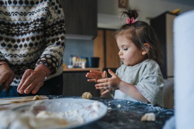 Küçük kız mutfakta yemek pişiriyor elleriyle hamur yoğuruyor annesiyle kurabiye hazırlıyor. Küçük kız, özenli annenin yardımıyla yemek yapmayı öğreniyor..