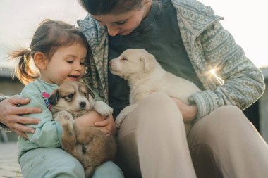 Mutlu küçük bir kızın portresi ve kucağında yavru köpekleri olan annesi. Birlikte güzel vakit geçiriyoruz. Aile kavramı, eğlence ve evcil hayvan mutluluğu. Hayvan sevgisi