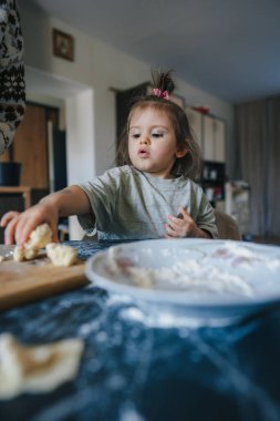 Dost canlısı küçük kızım modern mutfakta tatlı fırını pişiriyor ve kurabiye pişiriyor. Küçük kız, özenli annenin yardımıyla yemek yapmayı öğreniyor.