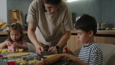 Mutlu aile annesi, küçük kızı ve oğlu birlikte yemek pişirirken mutfaktaki pasta malzemeleriyle eğleniyorlar.