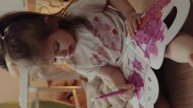 Evde yerde otururken pembe renkli kalemlerle çizen sevimli küçük kız. Çocuklar için eğitim faaliyetleri