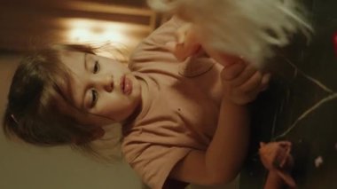 Evde oyuncak bebekle oynayan komik bir kız, bir bebeğe bakıyor, bebek bakıcılığı yapıyormuş gibi yapıyor. Mutfak oyuncakları simülasyonu, eğitim ve rol yapma oyuncakları