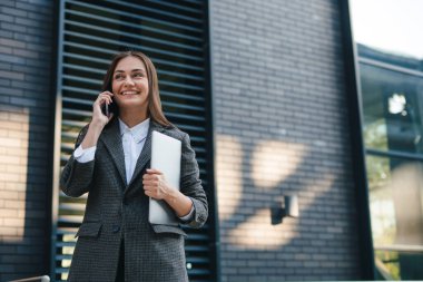 Diz üstü bilgisayarı olan bir iş kadını bina arkasında duruyor, cep telefonuyla konuşuyor, çağrıya cevap veriyor. Yaşam tarzı kavramı