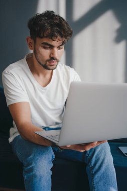 Oturma odasındaki kanepede otururken dizüstü bilgisayarda çalışan yakışıklı beyaz adam. Evden çalışan serbest çalışan biri. İnternet taranıyor.