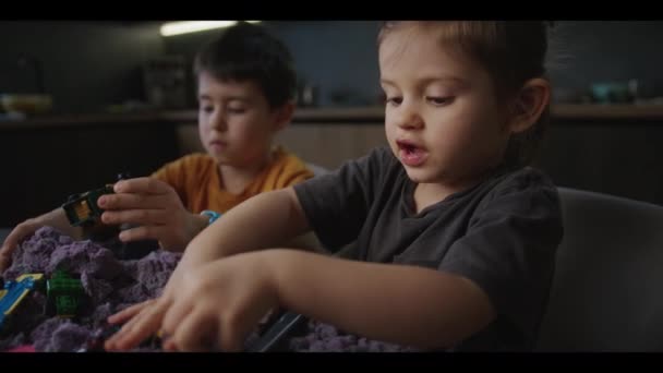 キッチンテーブルにプラスチックのおもちゃでキネティックな紫色の砂を遊んでいる兄と陽気な少女 幸せな子供時代を楽しんでいる 早期開発について ファインモータースキル — ストック動画