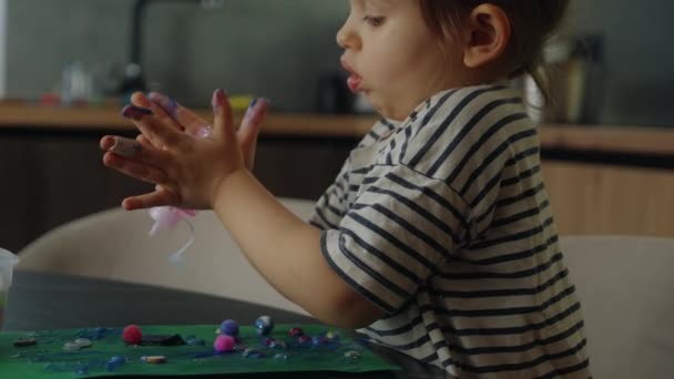 ピンクとブルーのグリッターの接着剤を自宅に座っている緑の紙に絞った小さな少女 部屋の机にカラフルな紙を貼っているかわいい子供たち ホーム — ストック動画