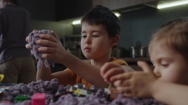 部屋のテーブルで紫色の運動的な砂で遊んでいる妹とかわいい少年 優れたモータースキルの開発 早期感覚教育について サンドアートセラピー — ストック動画