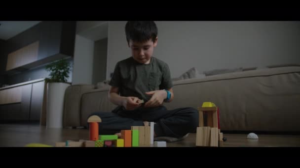 幼稚園の少年が木造建築ブロックからおもちゃの塔を建てて 自宅で床で遊んでいました デイケアコンセプト — ストック動画