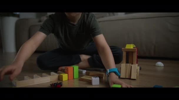 多色木製のブロックからビルディングコンストラクタータワーをプレイする小さな少年 自宅でフロアで楽しむこと — ストック動画
