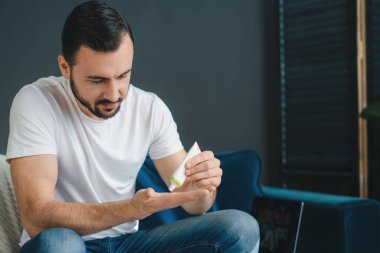 Adam kanepede oturuyor ve yüzüne sürmek için kremi tüpten avucuna döküyor. Sağlıklı yaşam tarzı.