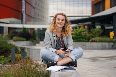 Cep telefonundan mesaj atan mutlu bir kadın laptopla dışarıda oturuyor. İyi haber konsepti