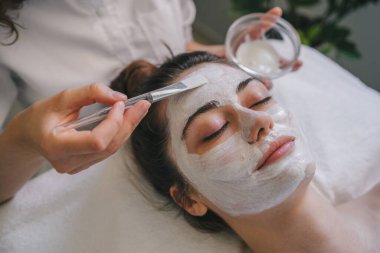 Kozmetikçiler cildini tazelemek için bir kadının yüzüne maske yapıyor. Kozmetoloji.