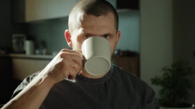 Elinde beyaz bir fincan kahveyle yalnız bir adam kameraya bakarken içiyor. Sağlık, özgünlük, denge ve sakinlik duygusu.