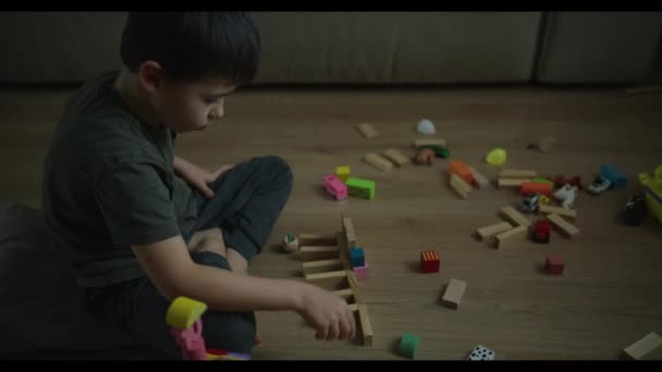 カラフルな木製のブロックで遊ぶ少数の慎重な少年は 床で一人で遊ぶ教育的なゲームを楽しんでいました 開発活動について キッズ 楽しむ — ストック動画