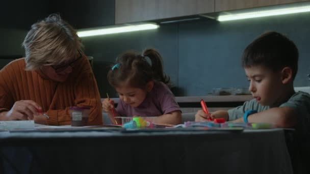 Mulher Idosa Alegre Duas Crianças Sentadas Mesa Desenhando Com Marcadores — Vídeo de Stock