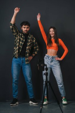 Güzel, gülümseyen genç bir çift siyah arka planda akıllı telefon kamerasıyla dans ediyor. Sosyal medya hesabı için popüler müzik içeriği videosu