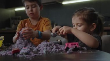 Mutlu çocuklar evde mor kinetik kumla ve araba oyuncaklarıyla oynuyorlar. Çocuklar için yaratıcı bir oyun, küçük çocuklarla karantina.