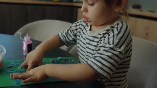 着色された綿球と青い輝く接着剤を使用して 彼女の両親に贈り物にカードを作ろうとしている愛らしい小さな慎重な少女 — ストック動画