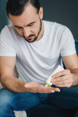 Adamın elleri evde oturan avuç içi parmaklarına beyaz tüpten krem sürüyor. Erkek derisi. Kozmetik ürünü. Nemlendirici tedavi.