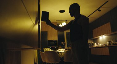 Loş ışıklı odada duran ve elini duvara doğru uzatan bir adamın siluetinin bir tarafından bak..