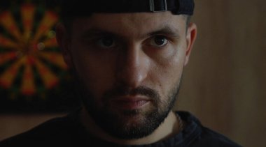 Kameraya dikkatle ve dikkatlice bakan vahşi bir adamın yakın plan portresi. Karanlık arka plan. İnsanlar ve duygular.