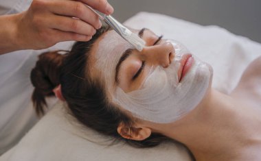 Güzellik salonunda güzellik uzmanı genç bir kadının yüzüne bakıyor. Yüz soyma maskesi, kaplıca güzellik tedavisi, cilt bakımı. Spa konsepti