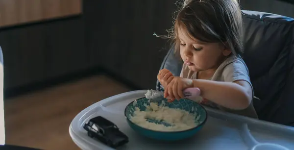 キッチンの小さな女の子は スプーンで熱心に米を食べる ストック画像
