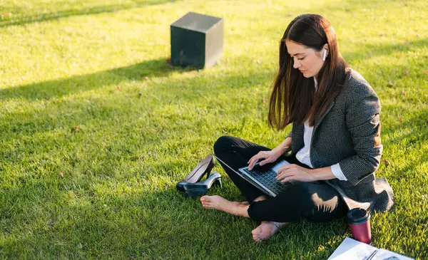 魅力的な若い女性の肖像画は オンライン屋外で働くラップトップを使用して夏の日に足で公園の緑の草の上に座っています 教育に関するコンセプト ストック画像