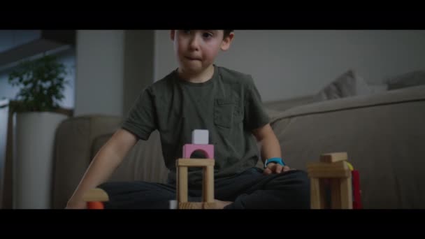 子供部屋に木製のキューブで建物を建てる床に座っている集中した幼稚園児のコンセプト — ストック動画
