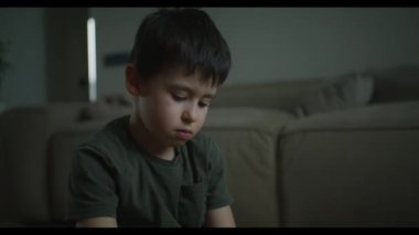 Kendine güvenen çocuk oturma odasında yerde oturan renkli ahşap tuğlalardan bir kule inşa ediyor. Çocuksu oda oyuncakları deposu