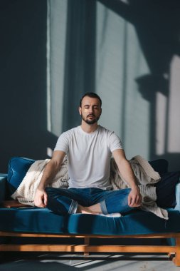 Nilüfer çiçeğinde meditasyon yapan, derin ve yavaşça nefes alan, rahat koçun üzerine oturmuş, evde dinlenen bir adam..