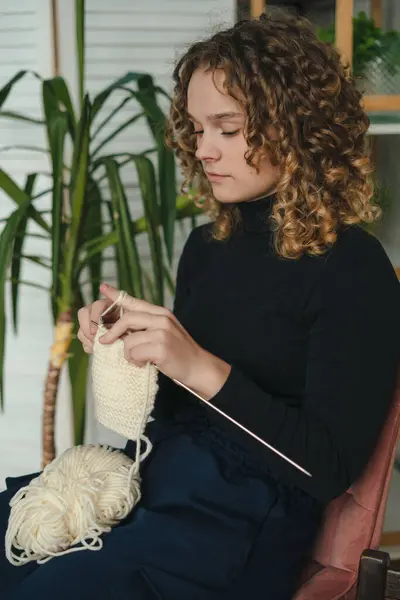 椅子に座っている自宅で白いニットの仕事を見ている若い女性 屋内趣味のレジャー活動の人 編み物の仕事について 一人で居心地の良い家で時間を過ごす女性 ロイヤリティフリーのストック写真