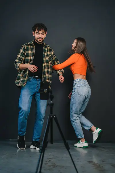 フォロワーのためのコンテンツを記録するミレニアル世代の男と女性 三脚に設定された携帯電話を使用して 黒い背景で踊り 微笑みます ストック写真