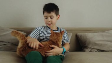 Evdeki kanepede sevimli kızıl kedisi olan küçük bir çocuk. Çocuk ve kedi. Çocuklar ve evcil hayvanlar.