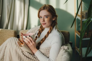 Pozitif odaklı edebiyat düşkünü kadın bir fincan çayla kanepede dinleniyor, kitap okuyor, hobilerinden keyif alıyor,.